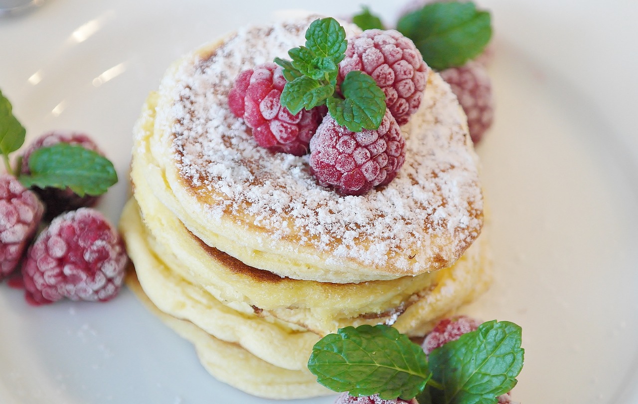 Pancake soffici alla ricotta decorati con frutta fresca e miele su un piatto elegante.